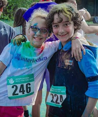 Two friends have their arms around each other and smile after a color run. Two friends have their arms around each other and smile after a color run.